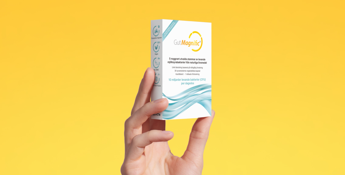 Hand som h&aring;ller en f&ouml;rpackning GutMagnific mot gul bakgrund.