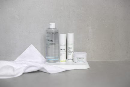 Bilden visar en upps&auml;ttning Dermaceutic hudv&aring;rdsprodukter, inklusive en flaska reng&ouml;rande micell&auml;rt vatten, tv&aring; behandlingsserum och en ansiktsmask, ordnade prydligt p&aring; en vit bricka med en vit handduk bredvid. Bakgrunden &auml;r neutral gr&aring;.