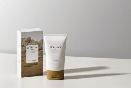 En tub med Skin1004 Centella hudv&aring;rdsprodukt st&aring;r bredvid sin f&ouml;rpackning p&aring; ett vitt bord. F&ouml;rpackningen har ett landskapsmotiv, och produkten har en enkel etikett med vit text.