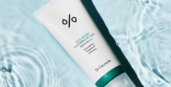 En vit tub med Dr. Ceuracles Cica Regen Waterproof Sun SPF50+ med en liggande p&aring; en bakgrund av bl&aring;tt vatten.