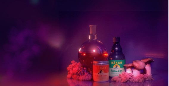 Produkter fr&aring;n H&auml;xan placerade bredvid en magisk flaska mot en lila dimmig bakgrund.