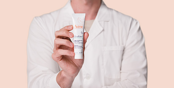 En person i vit laboratorierock håller upp en tub Avène Cicalfate+ kräm.